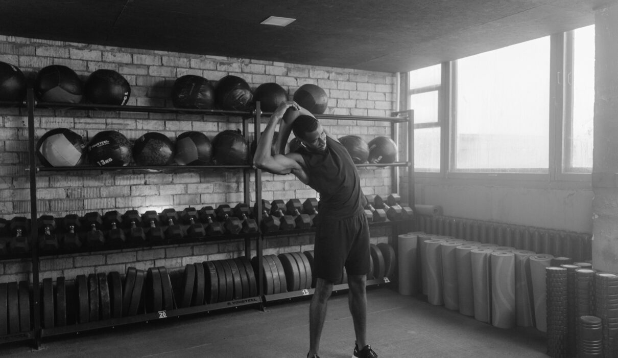 Man standing between treadmill and barbell in quiet gym, reflecting on cardio vs strength training