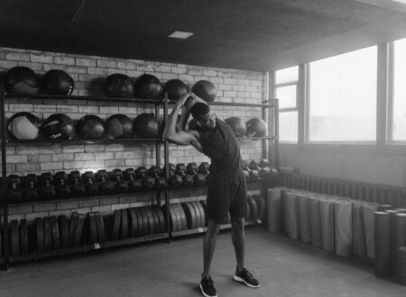 Man standing between treadmill and barbell in quiet gym, reflecting on cardio vs strength training