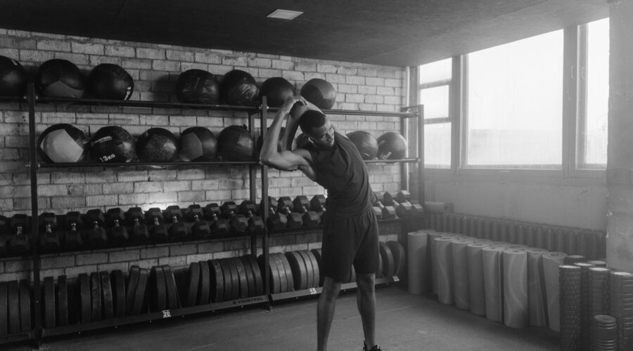Man standing between treadmill and barbell in quiet gym, reflecting on cardio vs strength training