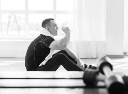 Man sitting alone on a gym bench after a workout under fluorescent lights, looking tired and reflective
