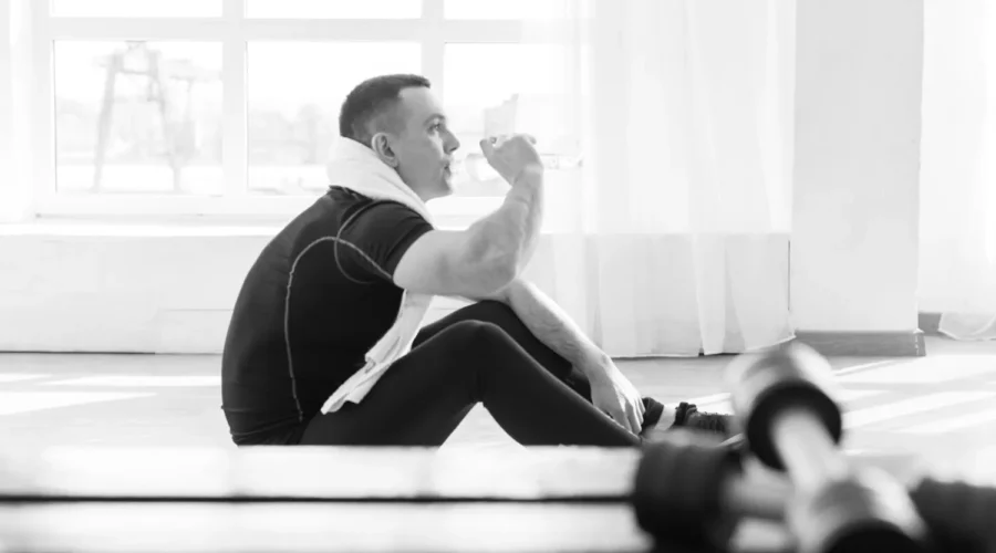 Man sitting alone on a gym bench after a workout under fluorescent lights, looking tired and reflective