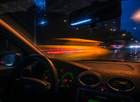 Man sitting alone in a parked car at night outside a gym, staring forward with tired expression and low interior lighting.