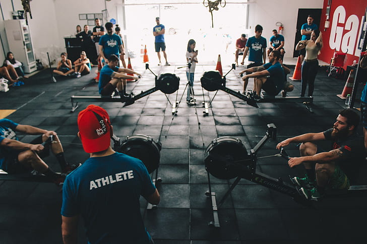 Crowded gym during evening hours with people lifting weights and one man looking visibly frustrated near a squat rack.