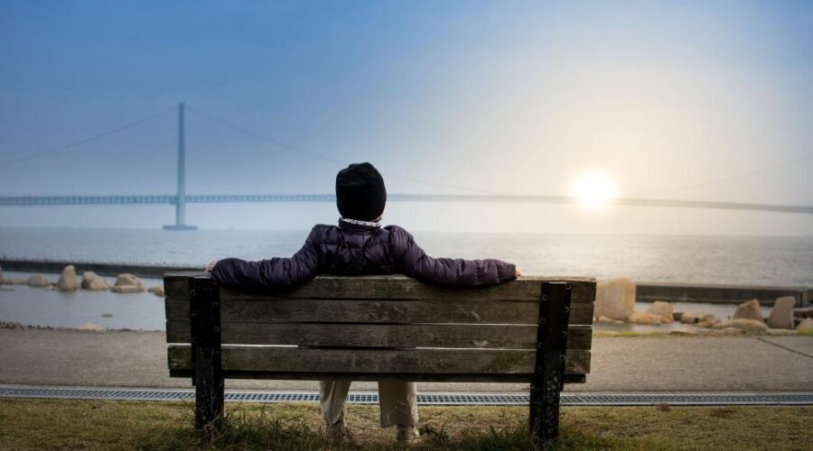 Person sitting quietly on park bench at sunrise reflecting on long-term lifestyle