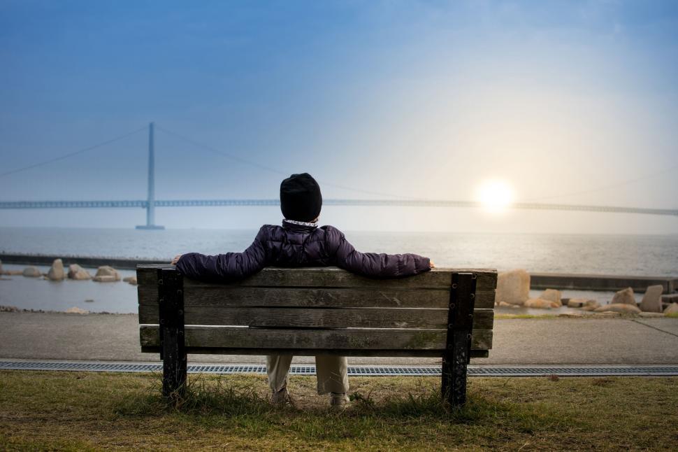 Person sitting quietly on park bench at sunrise reflecting on long-term lifestyle