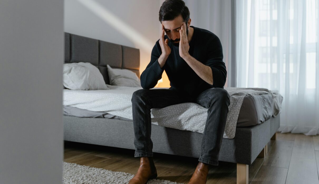 Person sitting on bed feeling mentally overwhelmed and exhausted