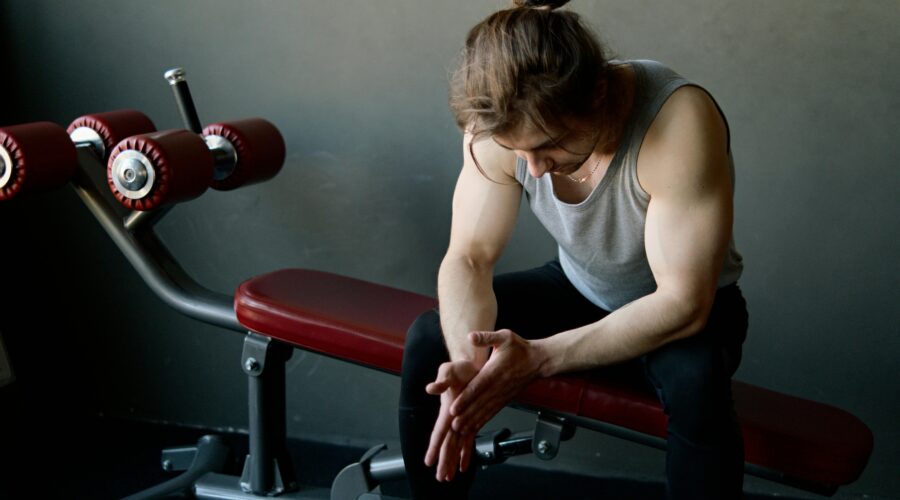 man sitting alone in gym looking tired and thoughtful about fitness consistency